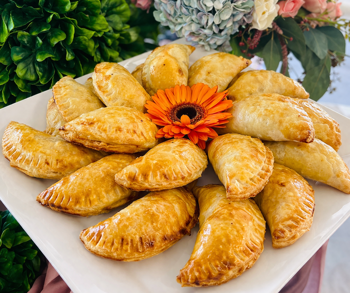 Golden empanadas arranged around an orange flower