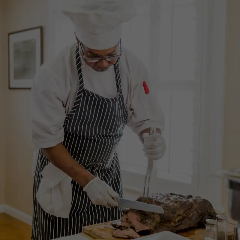 Chef carving roast beef on wooden board